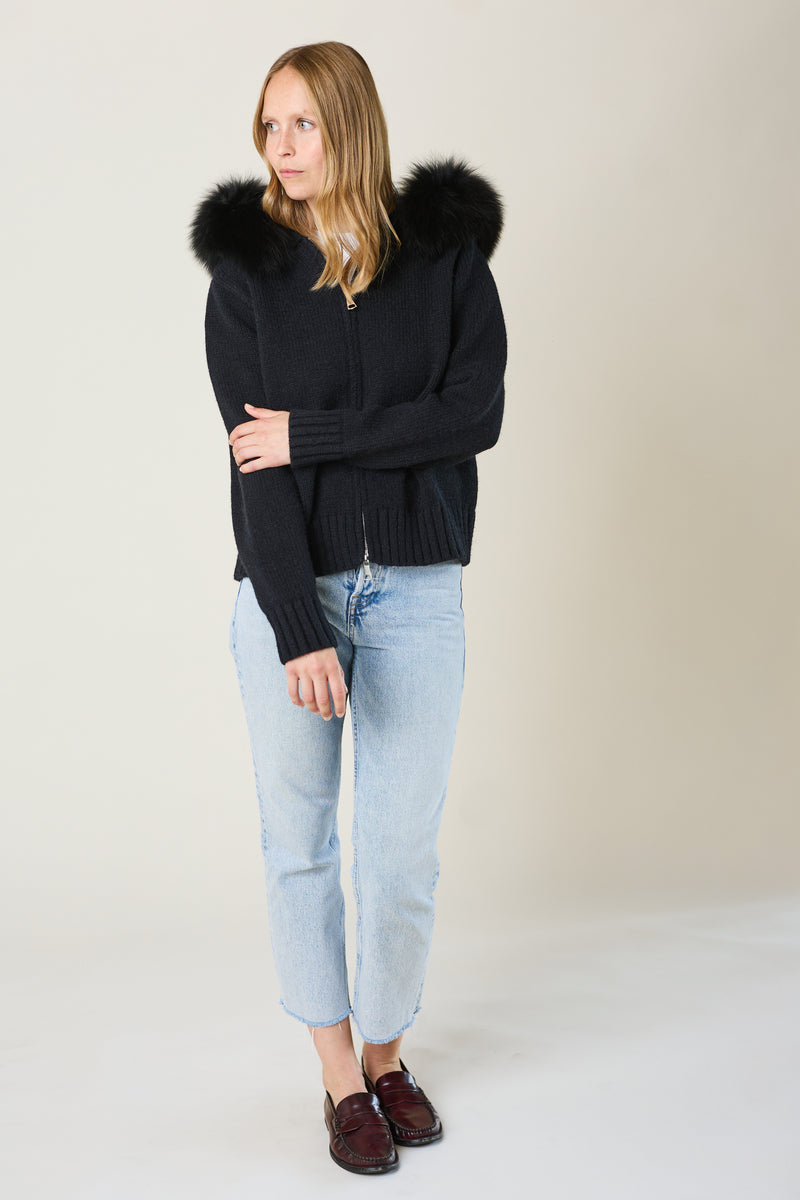 Woman wearing a black sweater with fur hood and light blue jeans on a white background
