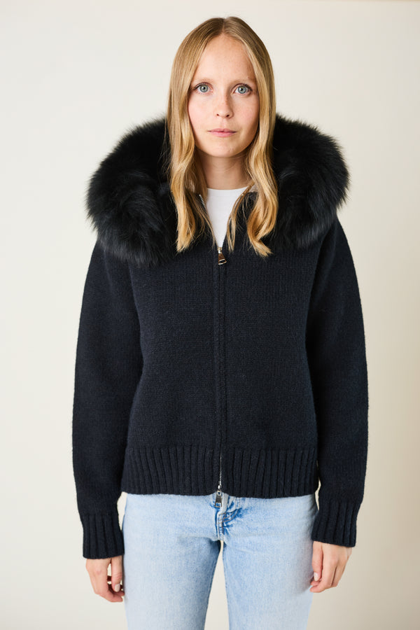 Woman wearing a black sweater with a fur hood against a plain background
