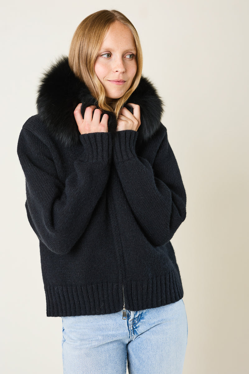 Person wearing a black sweater with fur collar against a plain background
