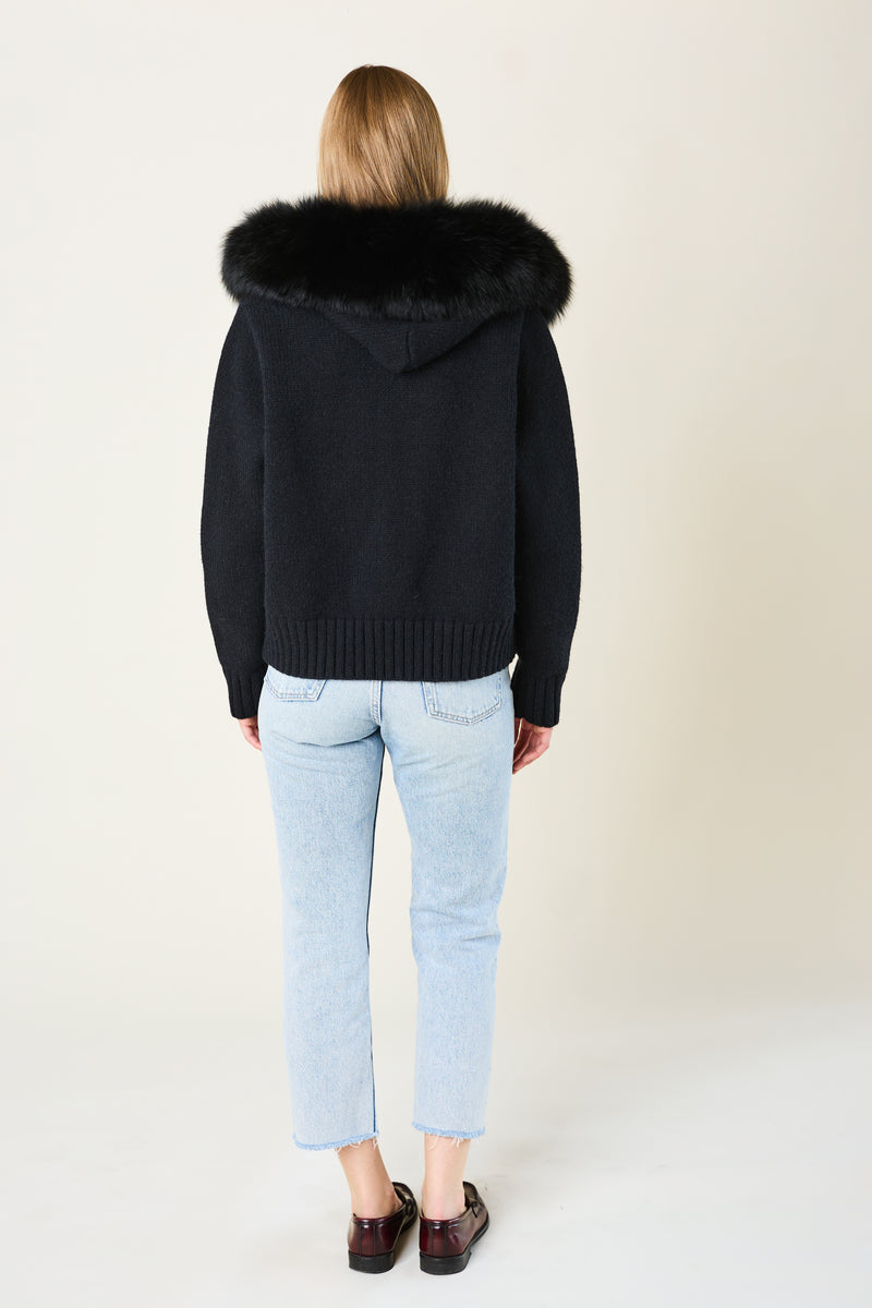 Person wearing a black hoodie with a fur-lined hood on a plain background