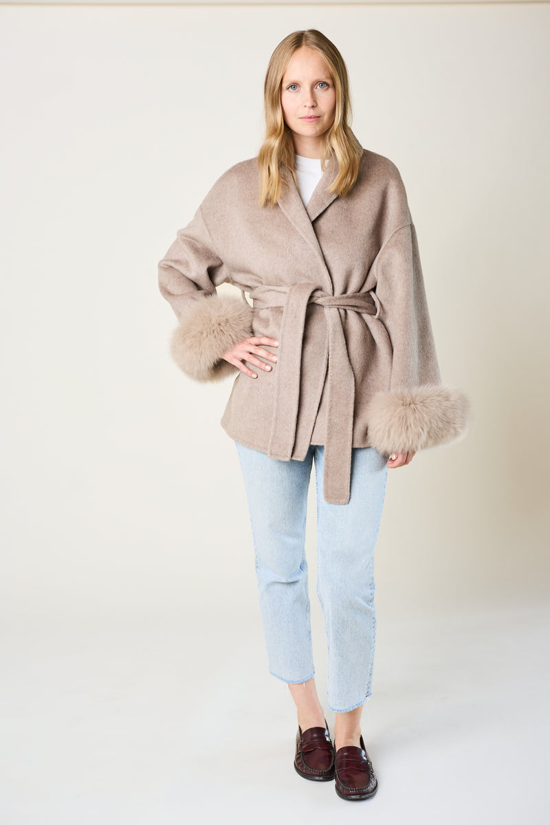 Woman wearing a beige coat with fur trim on a white background