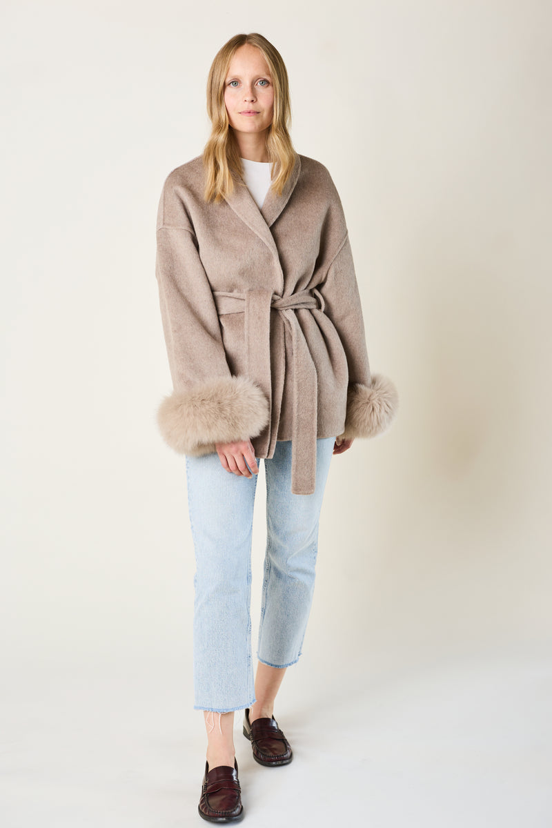 Woman wearing a taupe coat with fox fur cuffs on a plain background