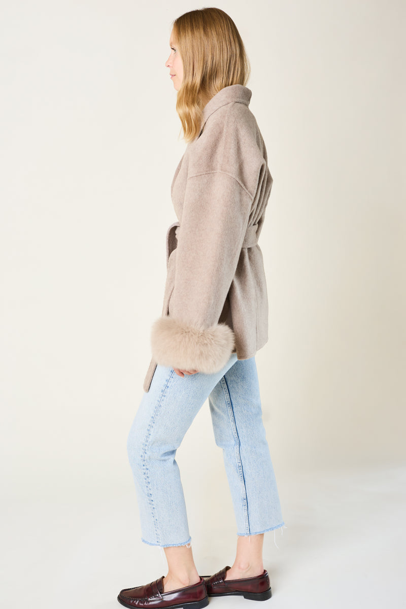 Woman wearing a beige coat with real fur trim on a plain background