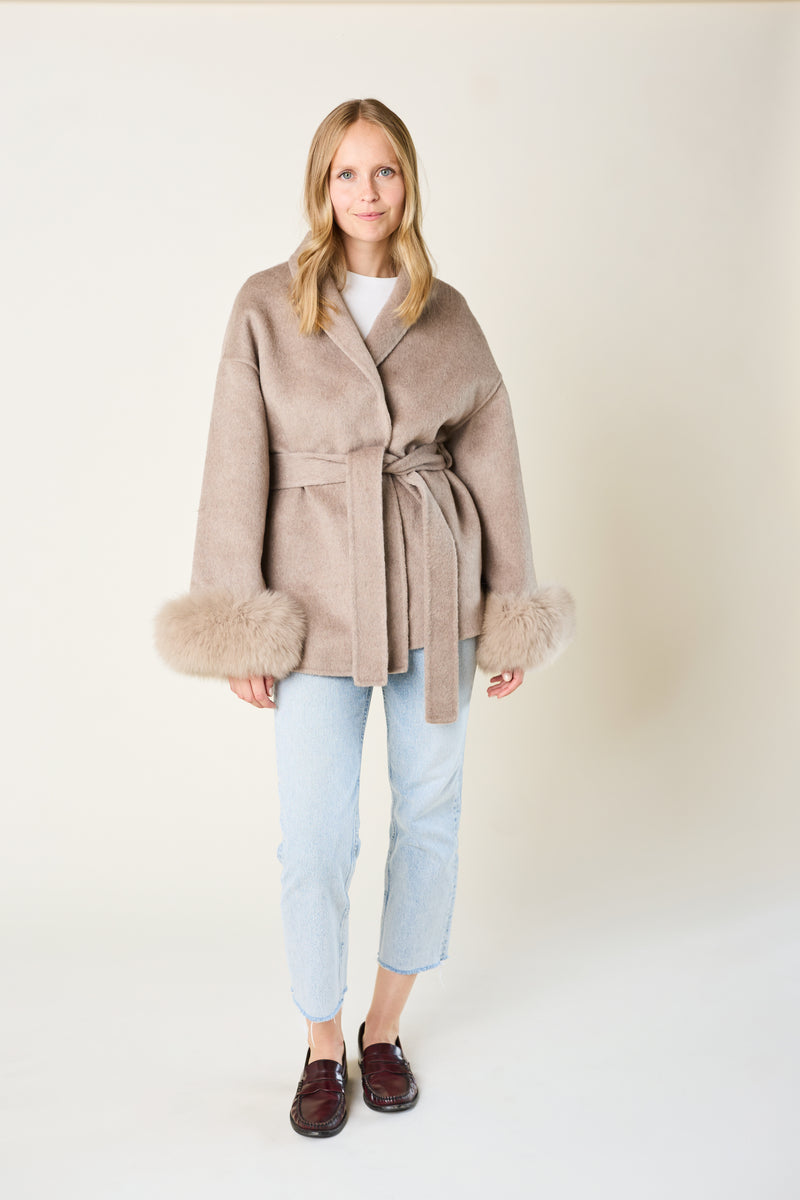 Woman wearing a beige coat with fur trim on a plain background
