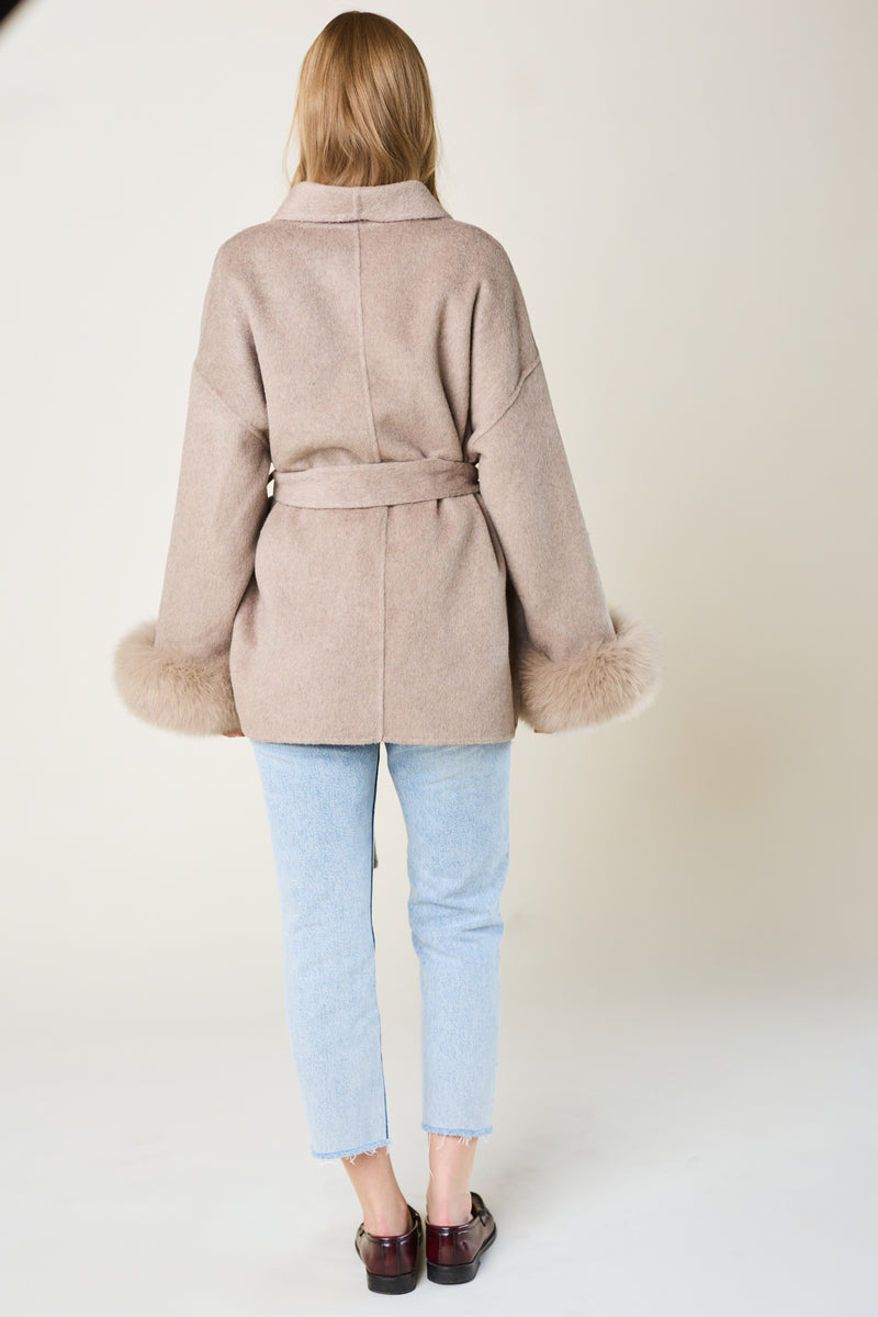 Person wearing a beige coat with fur trim on a white background