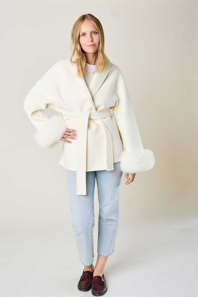 Woman wearing a white coat with fur trim on a plain background