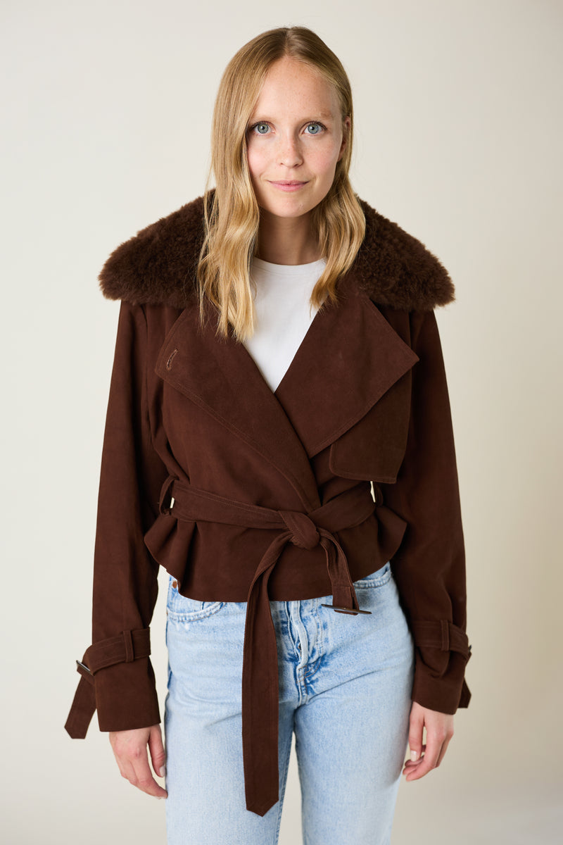 Woman wearing a brown coat with fur collar against a plain background