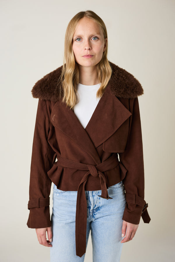 Woman wearing a brown coat with fur collar against a plain background