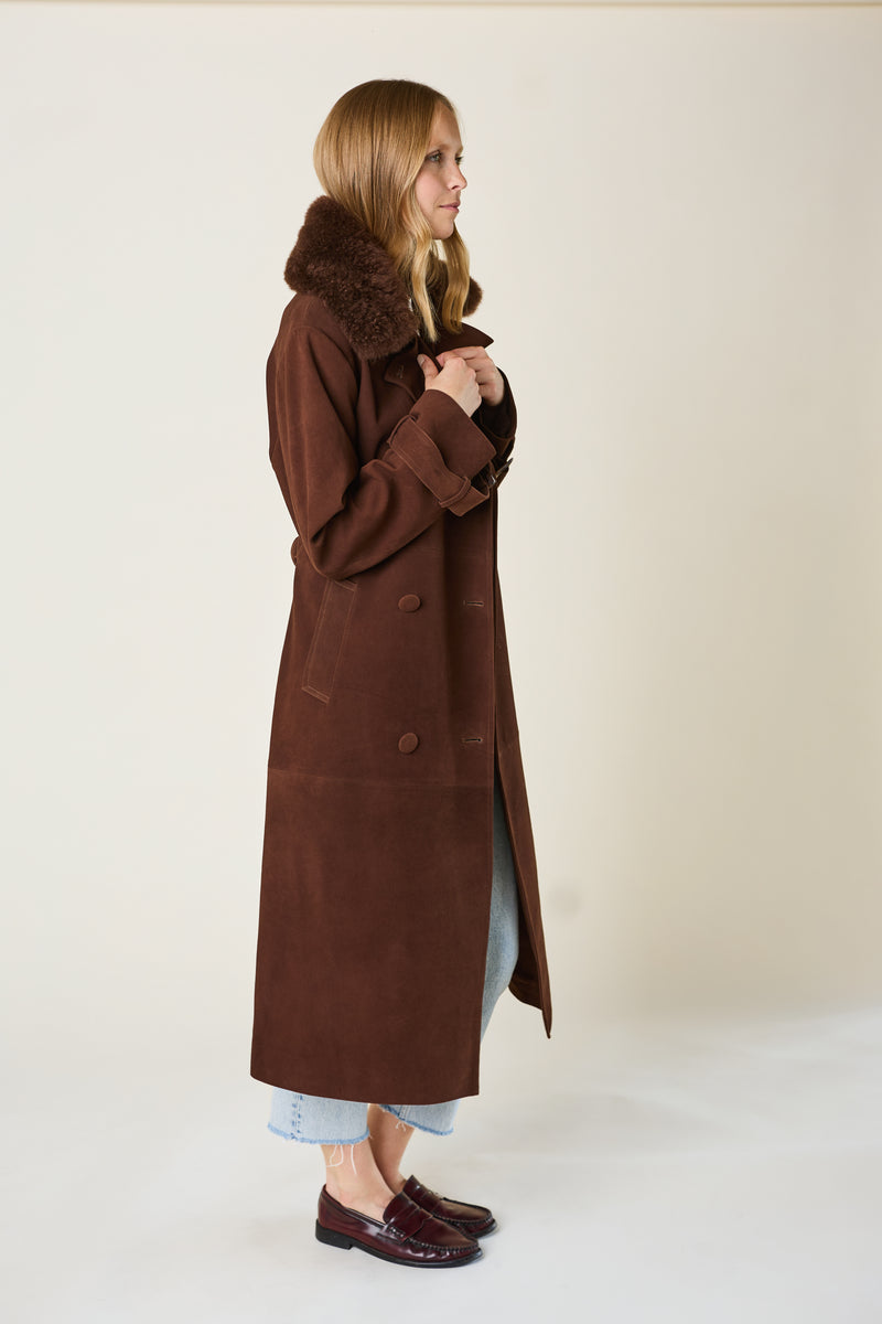 Woman wearing a long brown coat with fur collar on a plain background