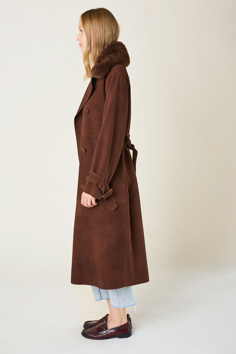 Woman wearing a long brown coat with fur hood on a plain background