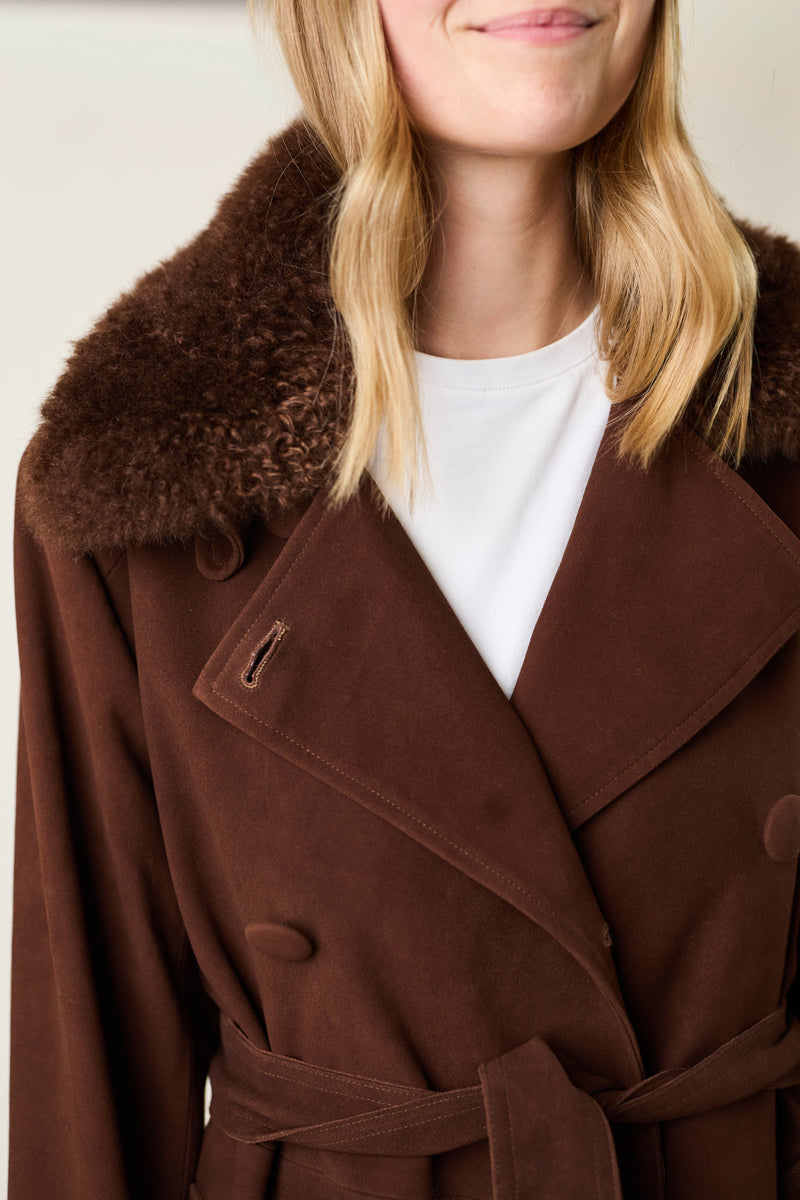 Brown coat with fur collar worn by a person against a neutral background