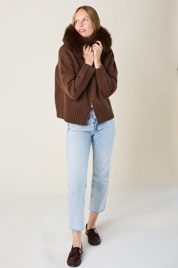 Woman wearing a brown sweater with a fur collar and light blue jeans on a white background