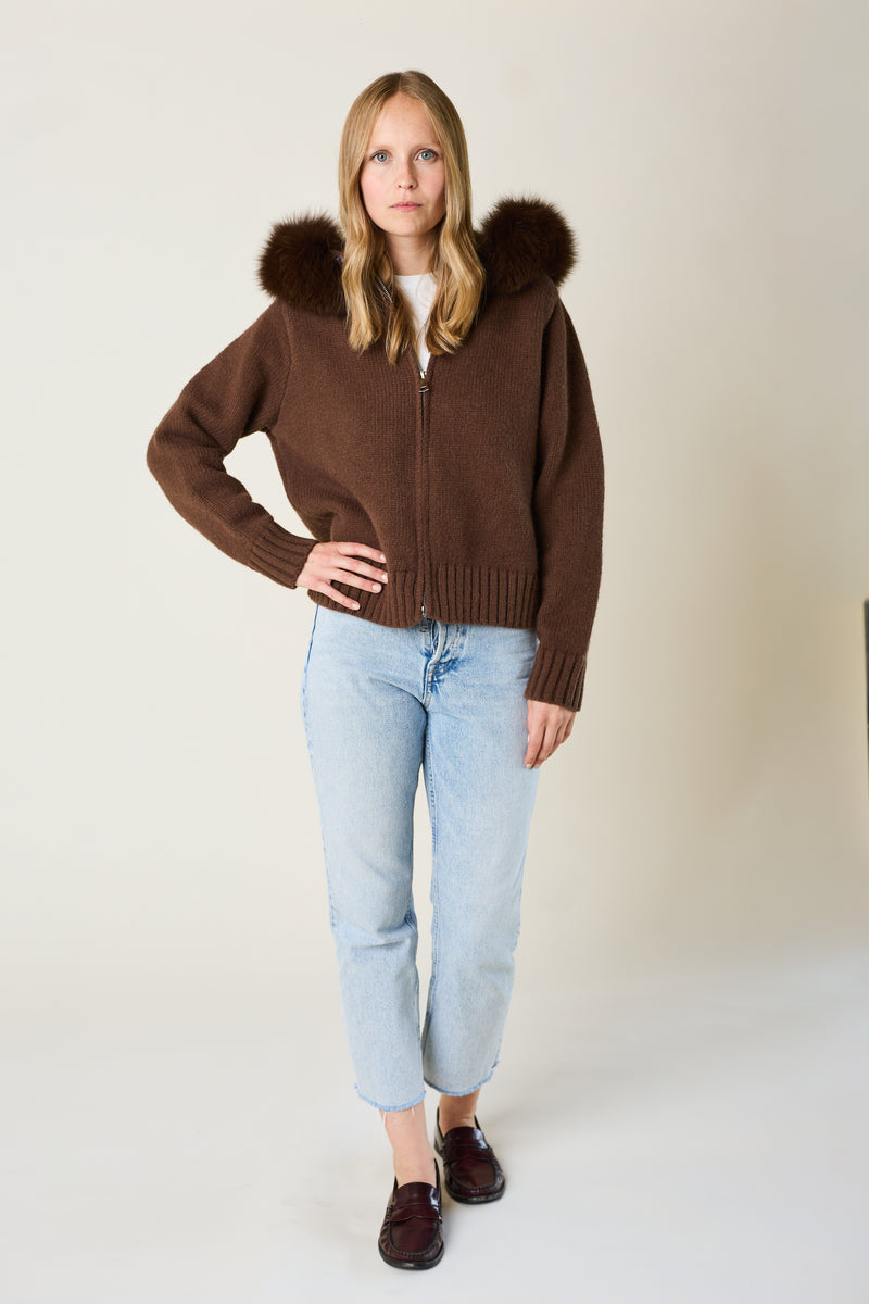 Woman wearing a brown sweater with fur hood against a plain background