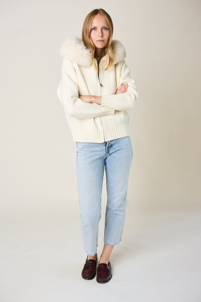 Person wearing a cream-colored cardigan, light blue jeans, and brown shoes on a plain background