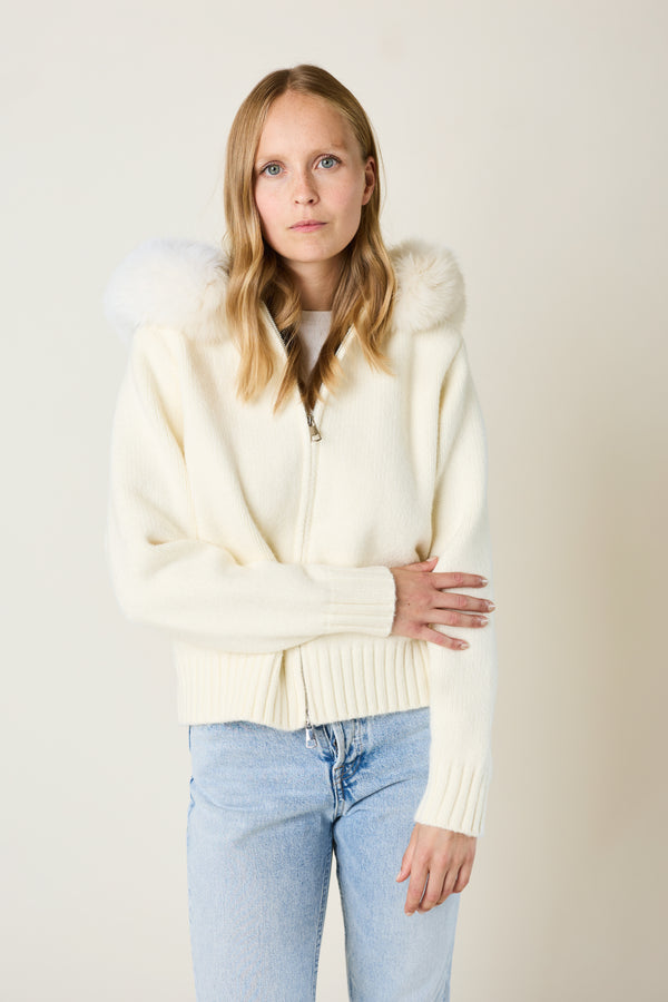 Woman wearing a cream-colored cardigan with fur trim against a plain background