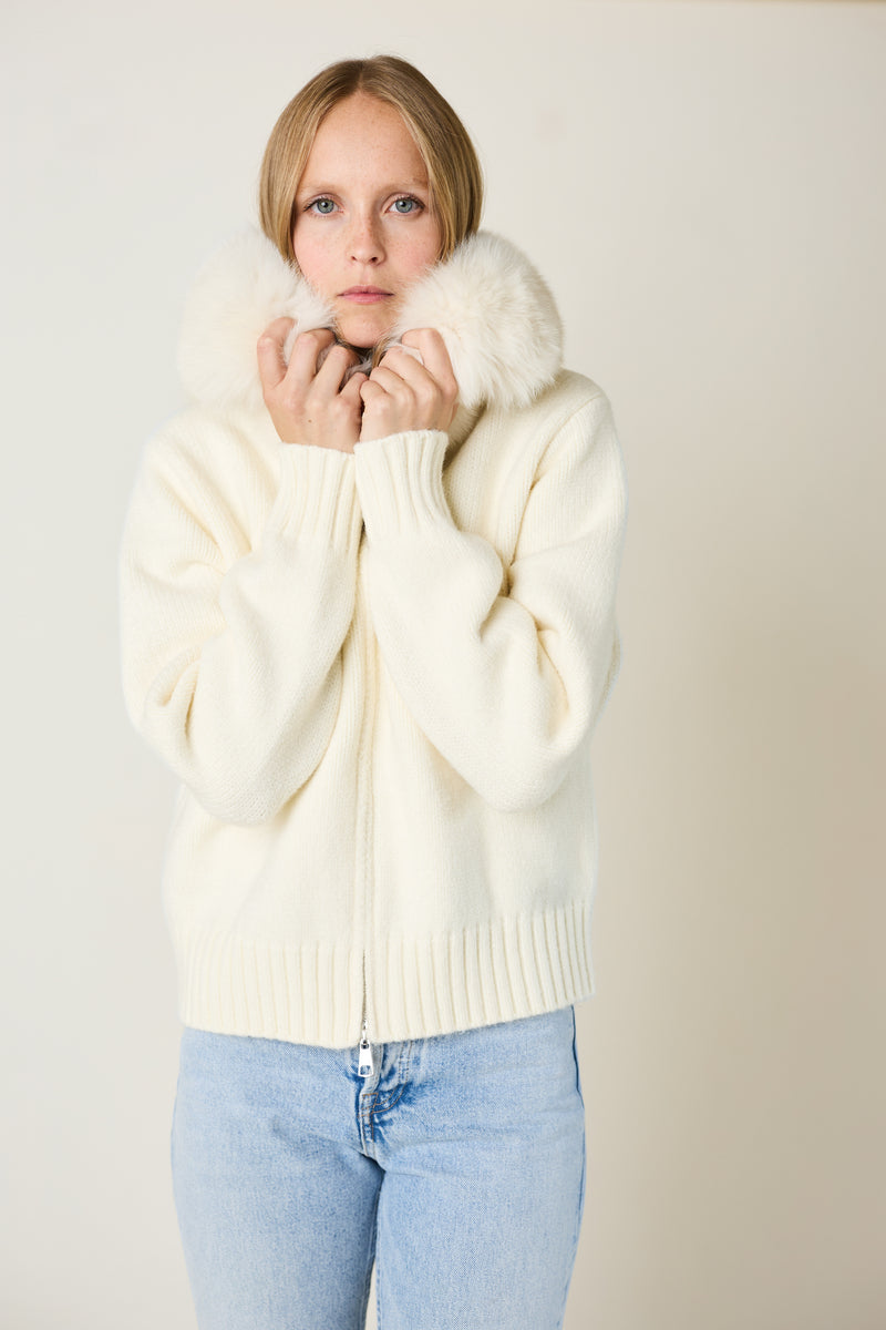 Woman wearing a cream sweater with fur trim against a plain background