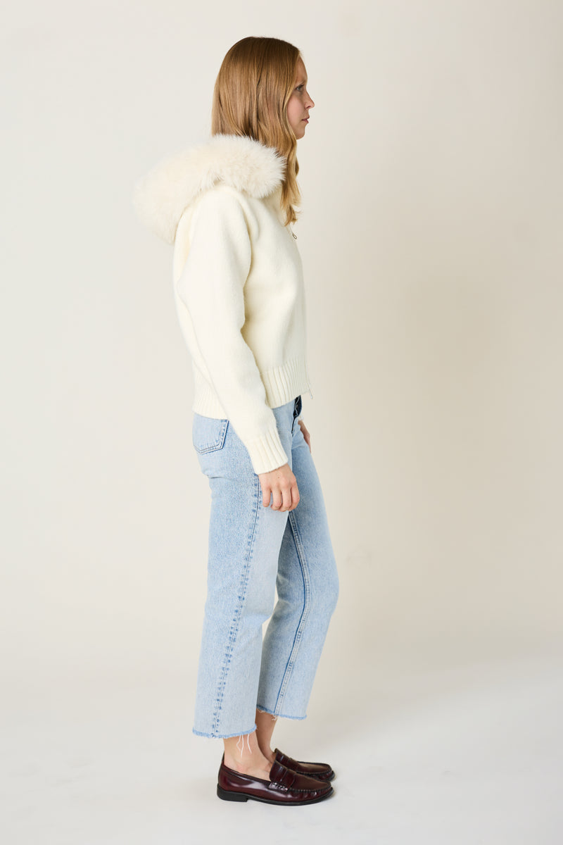 Woman wearing a cream sweater and light blue jeans on a plain background
